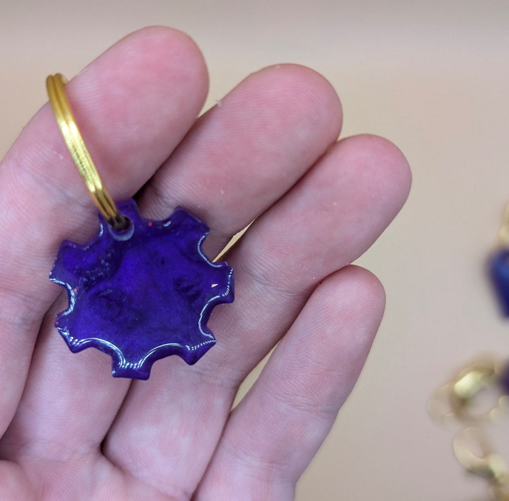 Purple keychain with gold ring held in a hand against a beige background