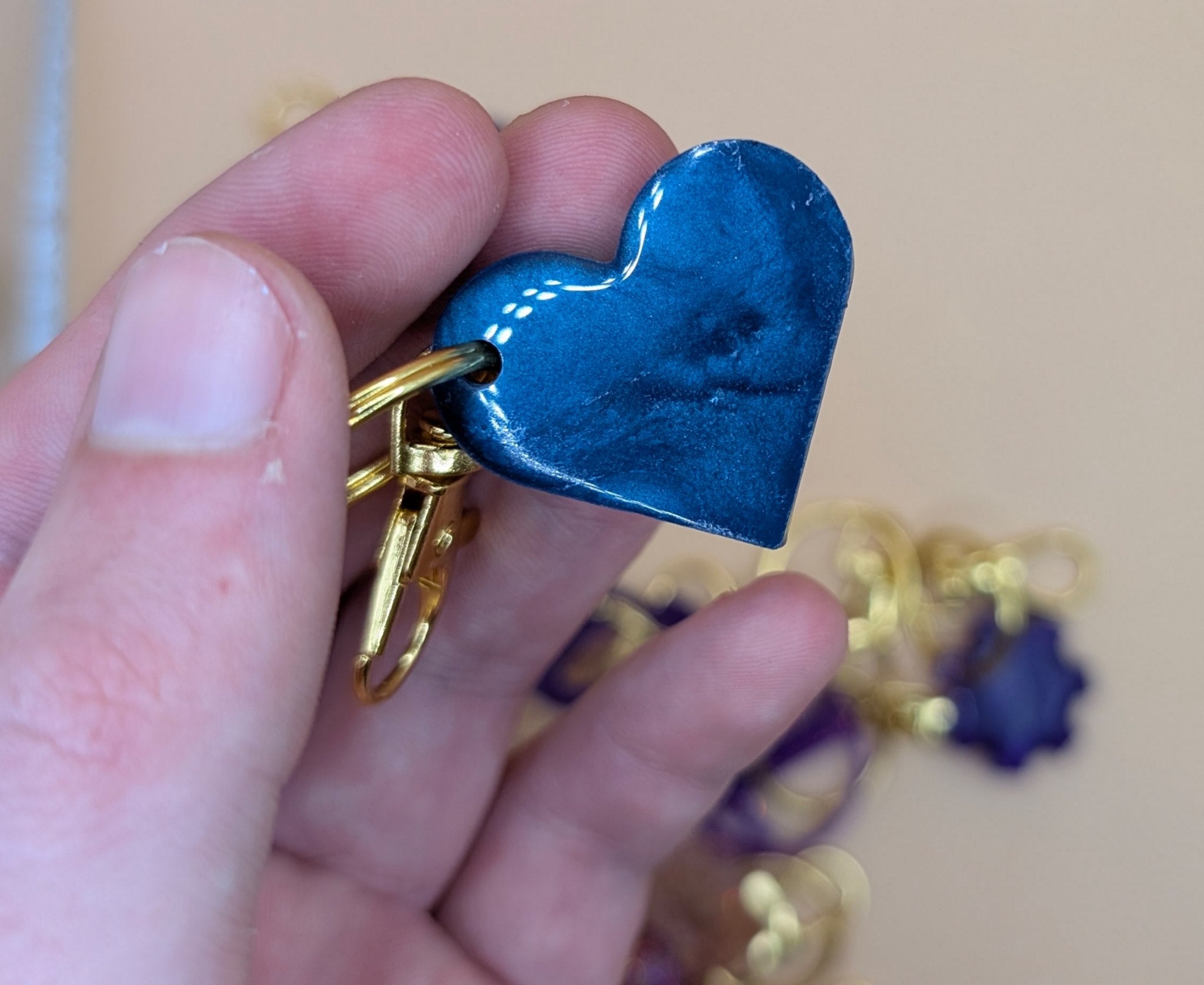 Hand holding a blue heart-shaped keychain with a gold clasp against a beige background