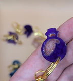 Purple keychain with gold accents held in a hand against a blurred background